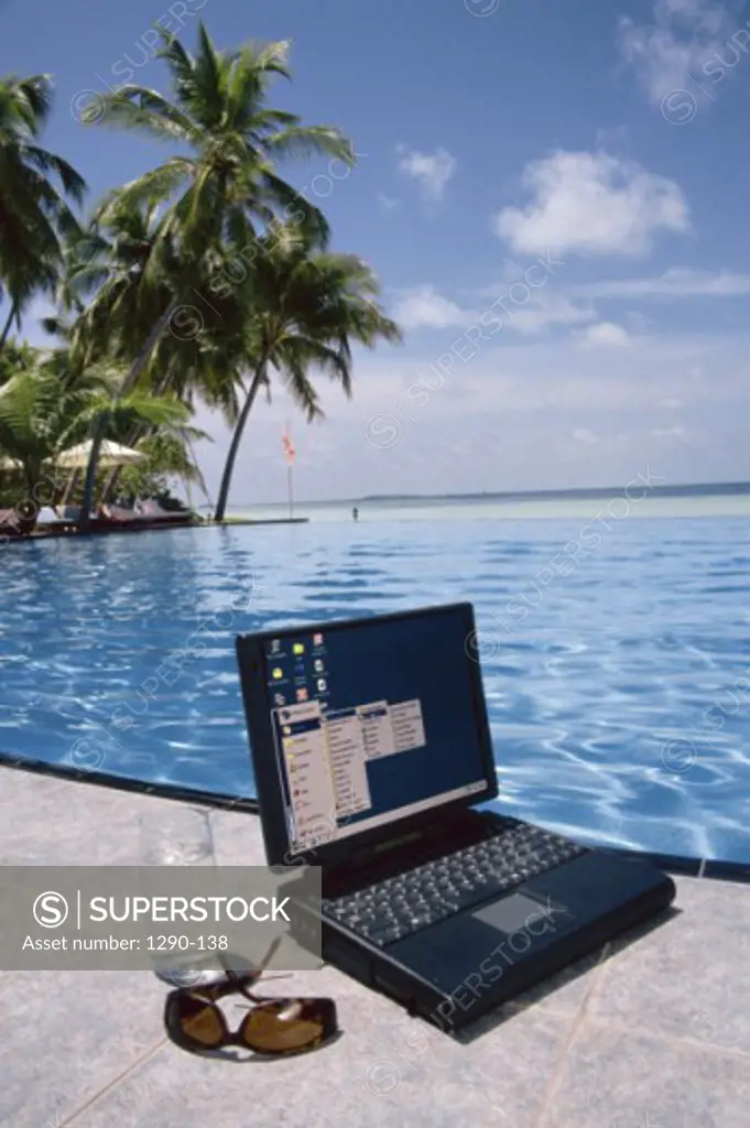 Close-up of a laptop and sunglasses at poolside