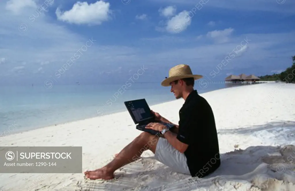 Side profile of a young man using a laptop on the beach