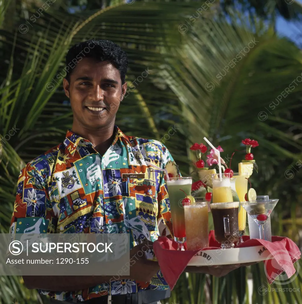 Portrait of a young man holding cocktails on a tray