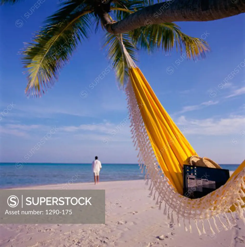 Laptop and a straw hat in a hammock with a businessman walking on the beach in the background