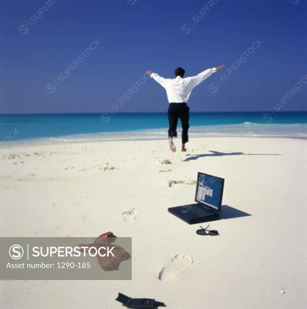 Laptop and a mobile phone on the beach with a businessman running in the background