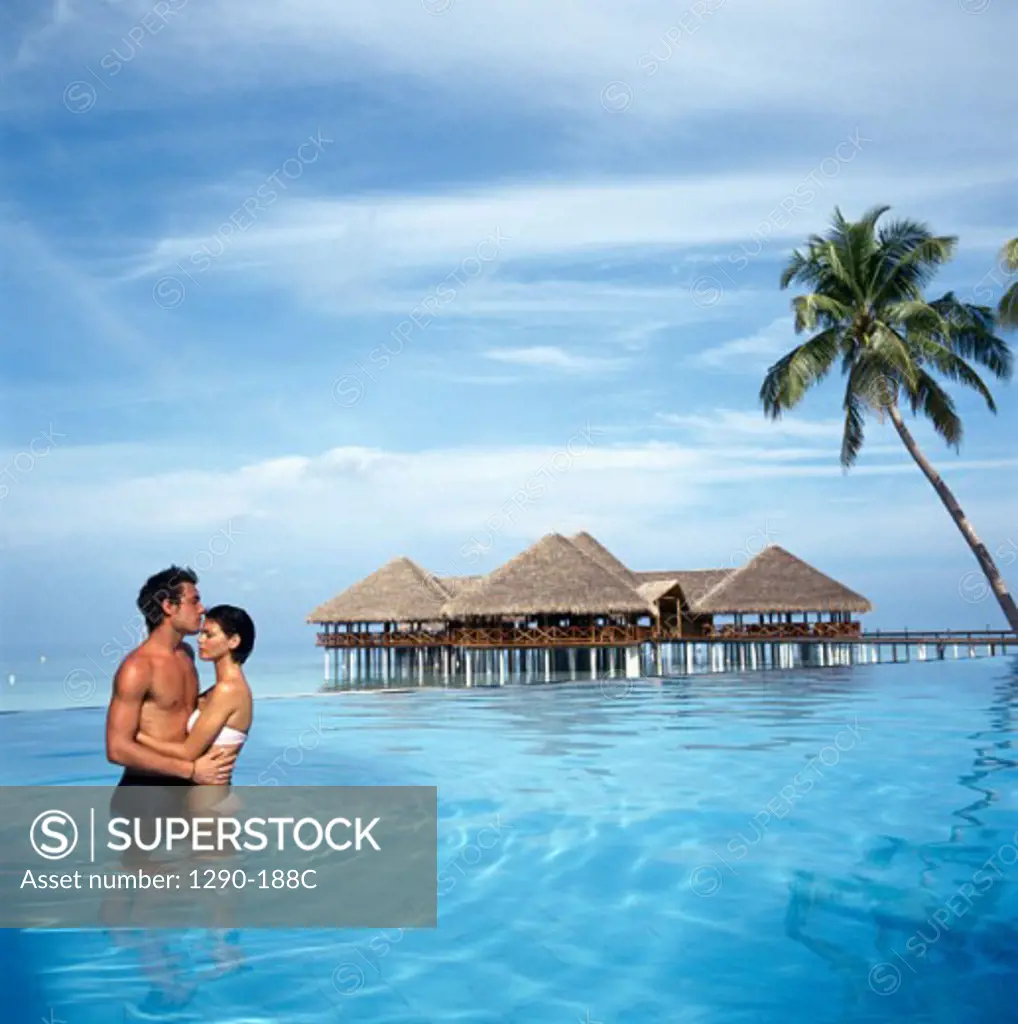 Side profile of a young couple standing in water and embracing each other, Maldives