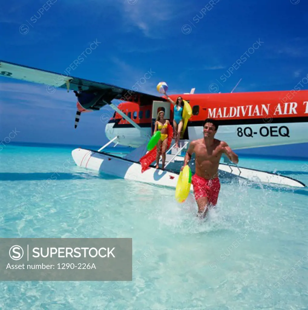 Young man running in water with two young women standing on a seaplane behind him, Maldives