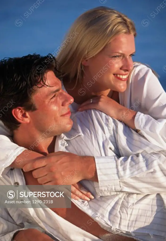 Close-up of a young woman embracing a young man from behind on the beach