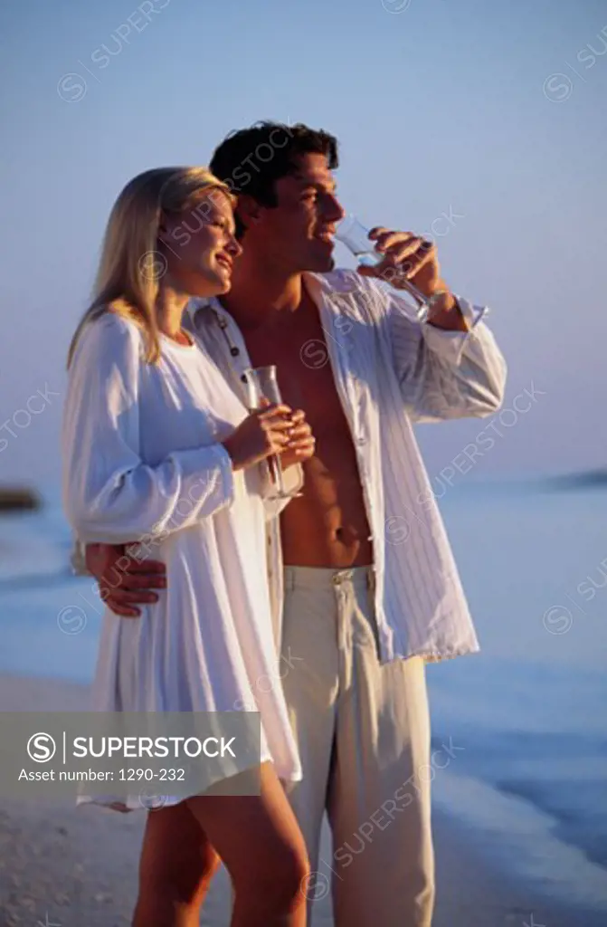 Young couple standing on the beach and drinking champagne