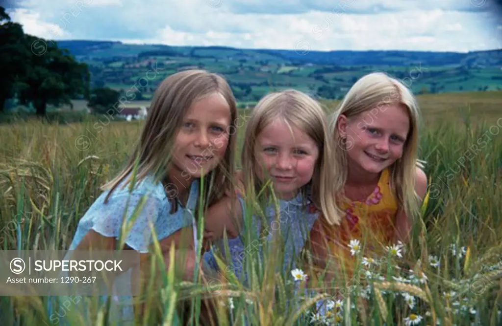 Portrait of three girls squatting in a field and smiling