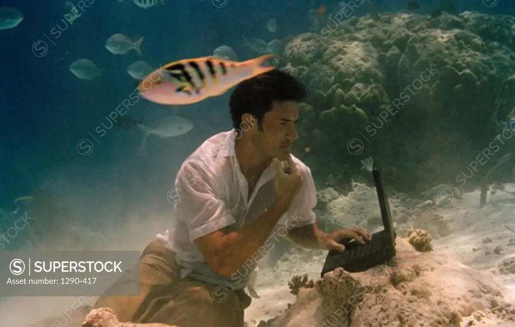 Young man sitting underwater and using a laptop