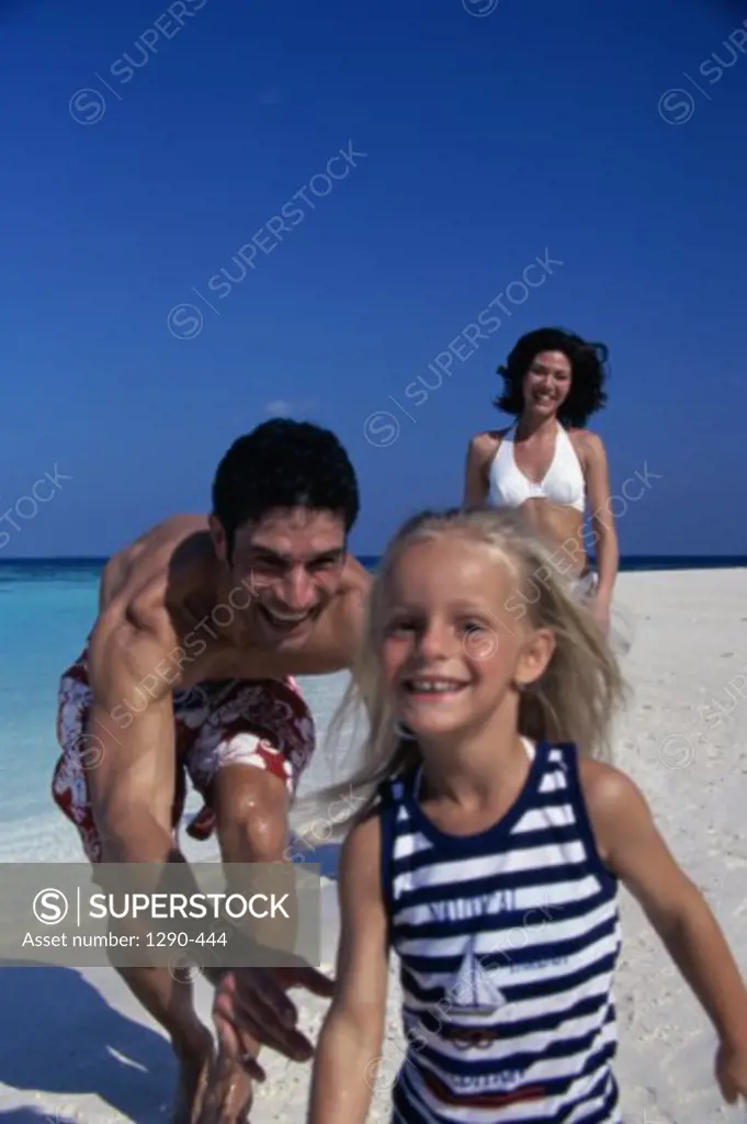 Young couple running behind their daughter on the beach