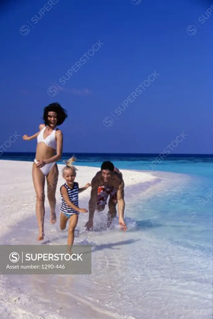 Young couple with their daughter running on the beach