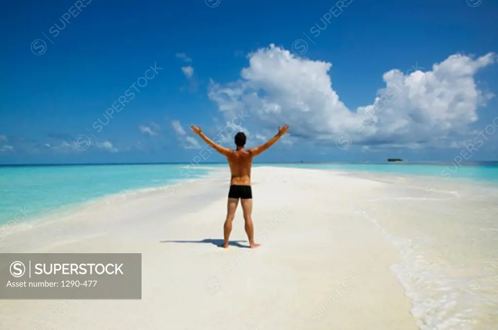 Rear view of a young man standing on the beach with his arms outstretched, Maayafushi, Maldives