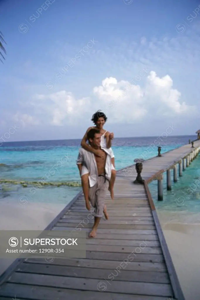 Young woman riding piggyback on a young man at a pier, Maldives