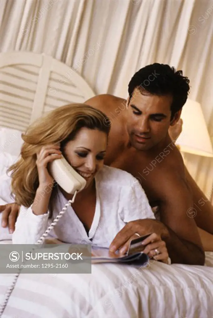 Young woman talking on the telephone and a young man lying behind her