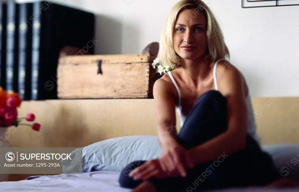 Portrait of mid adult woman sitting on bed, lookng at camera and smiling