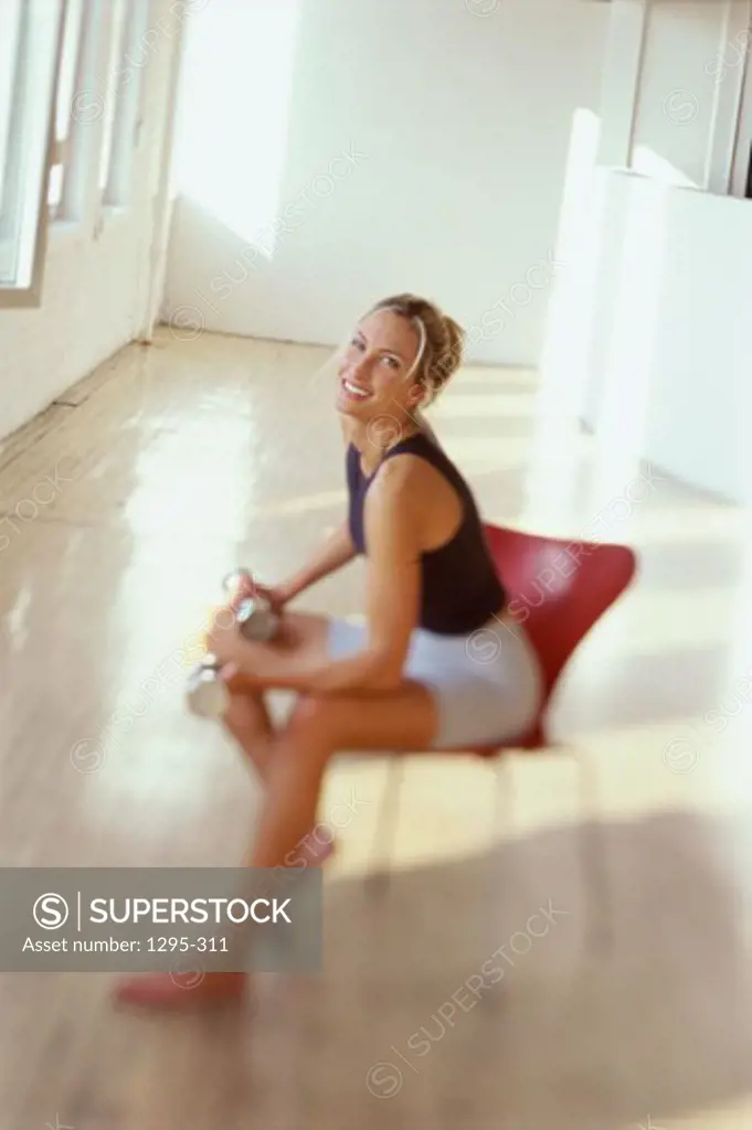 Young woman sitting on a chair holding a dumbbell smiling