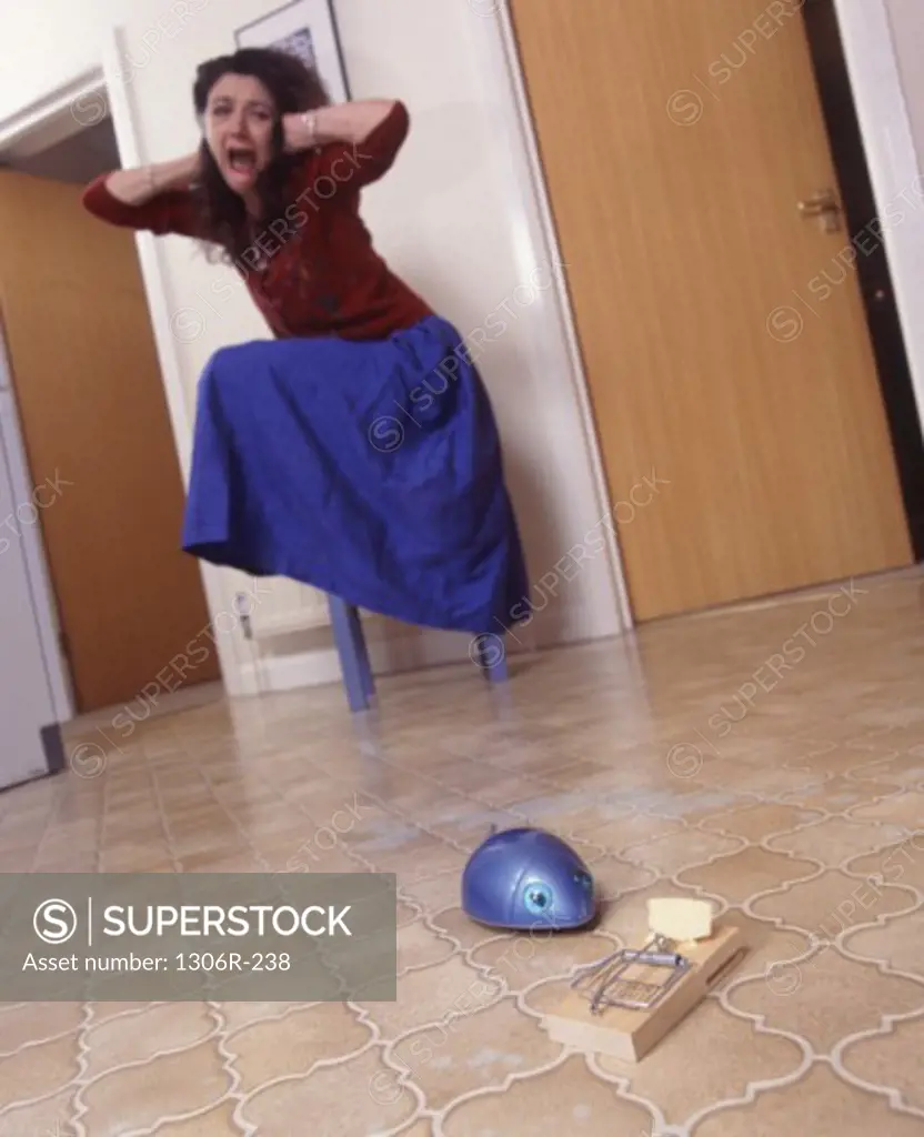 Low angle view of a woman on a stool afraid of a computer mouse on the floor near a mousetrap