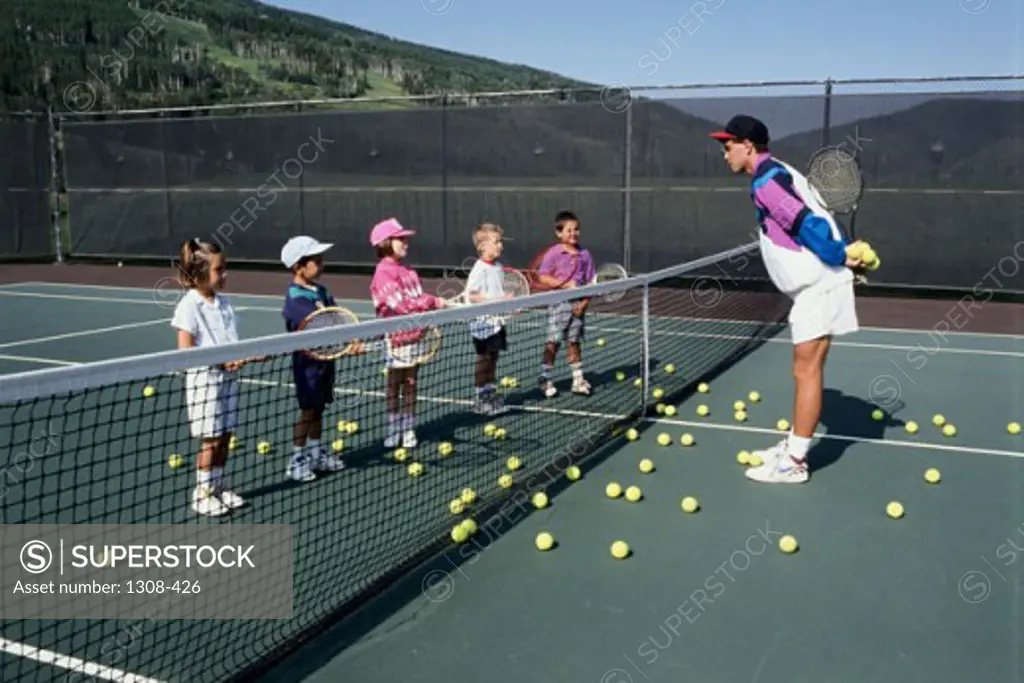 Boys and girls with their coach on a tennis court