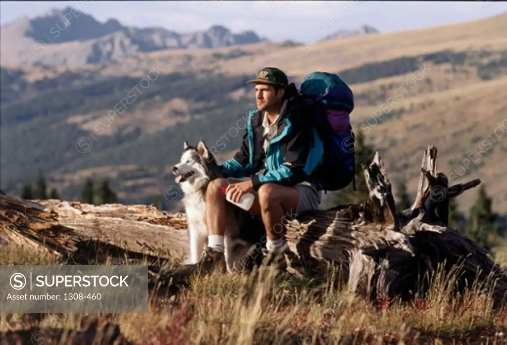 Young man sitting on a log with his dog, Vail, Colorado, USA