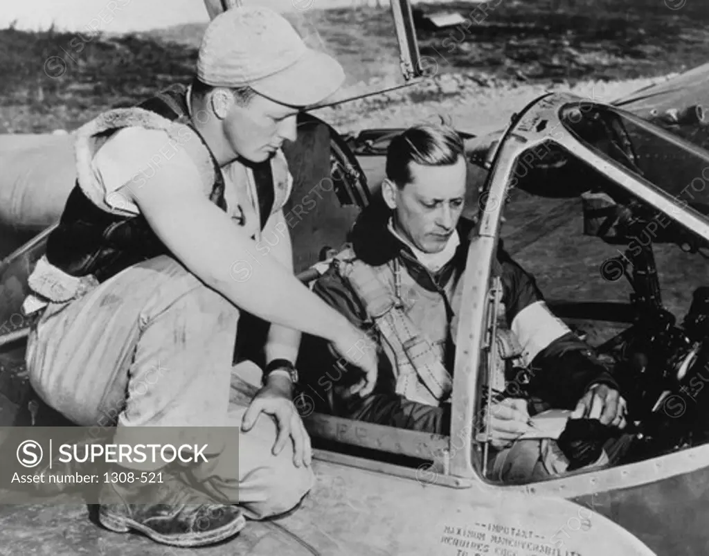 Close-up of a young man kneeling near a fighter pilot on a plane, 1940s