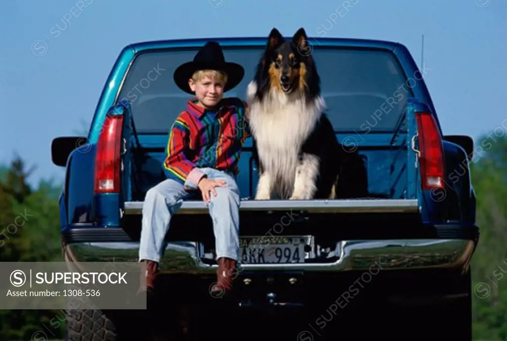 Portrait of a boy sitting with his dog in a pick-up truck