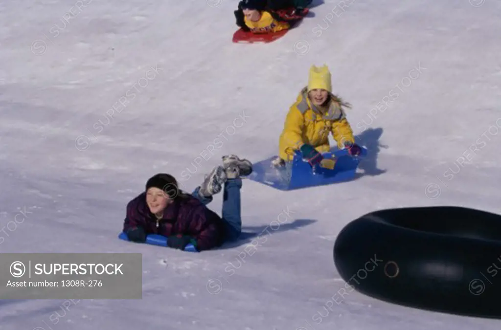 Two girls and a boy sledding on snow