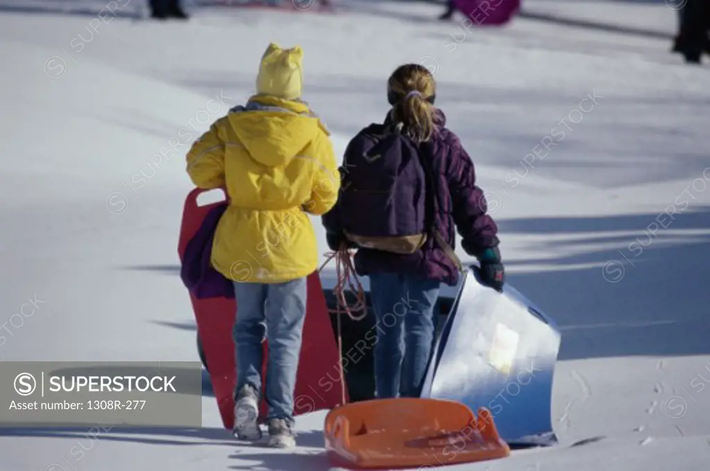 Rear view of two girls walking with sleds