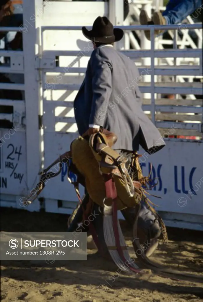 Cowboy at a rodeo carrying a saddle