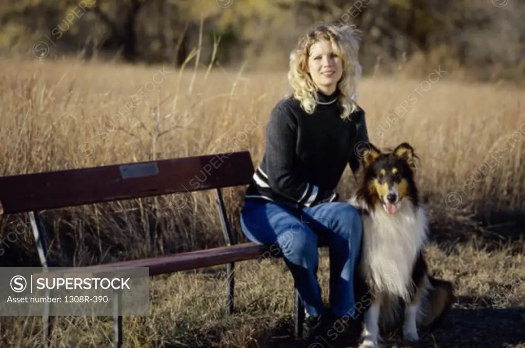 Portrait of a young woman sitting on a park bench with her dog