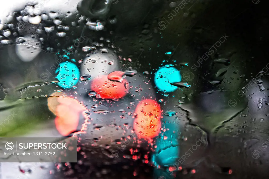 Tailights, traffic signals and rain drops help create an artistic look through the winsshield of a car.