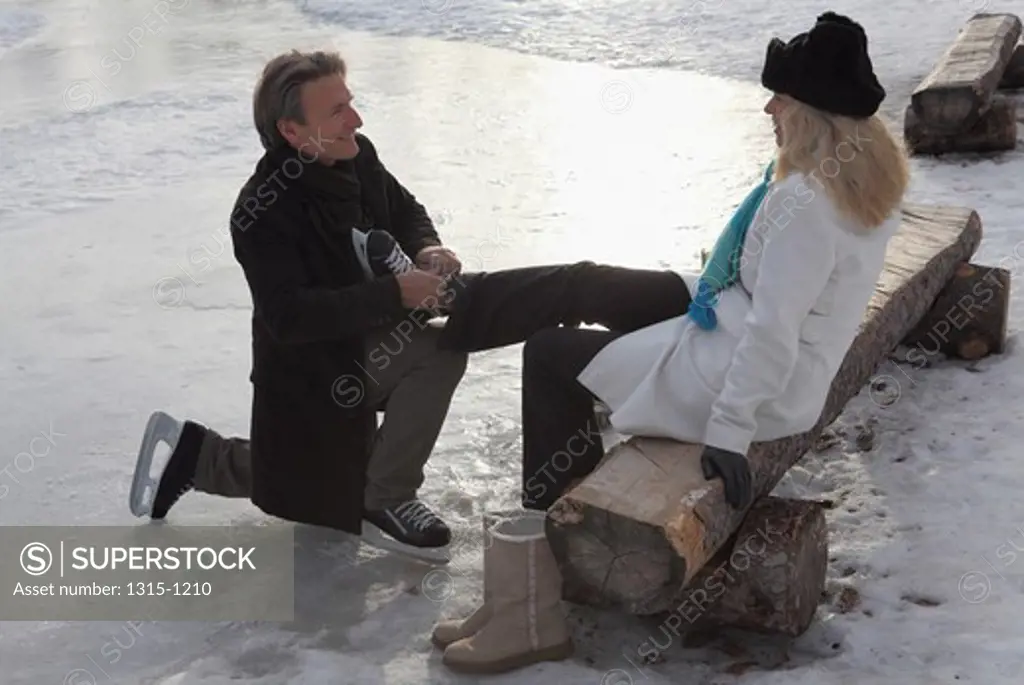 Mature man putting on ice skate to his wife, Alberta, Canada