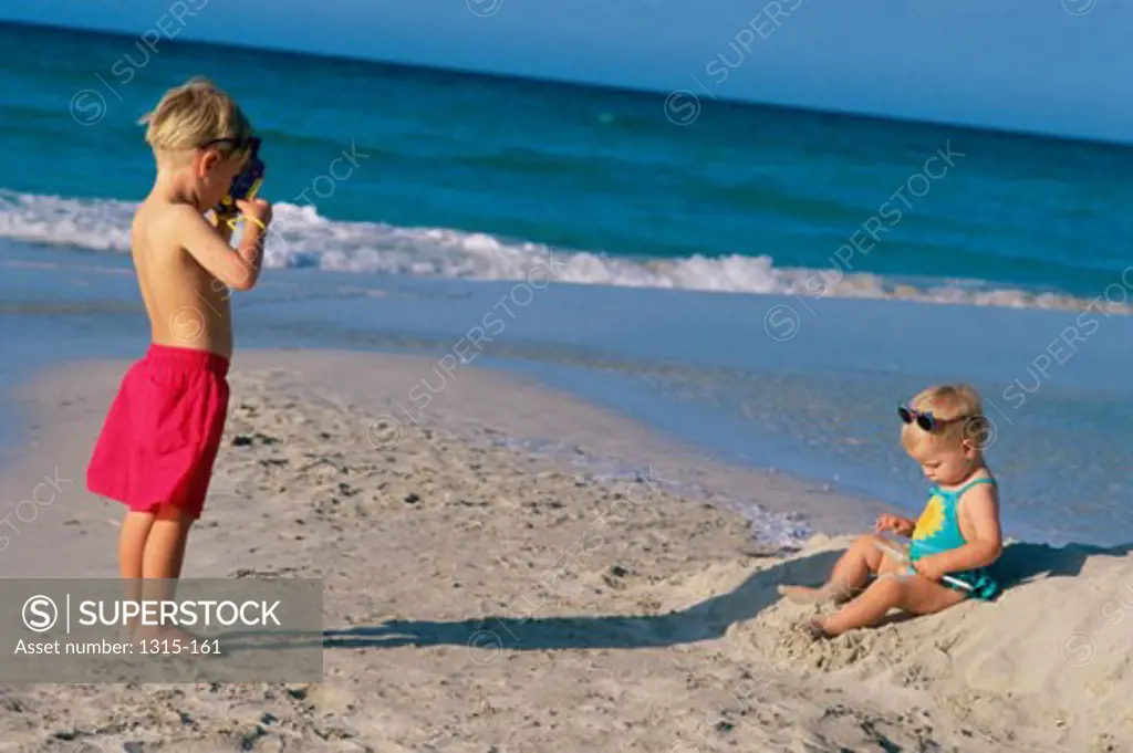 Side profile of a brother taking a photograph of his sister on the beach, Varadero Beach, Cuba