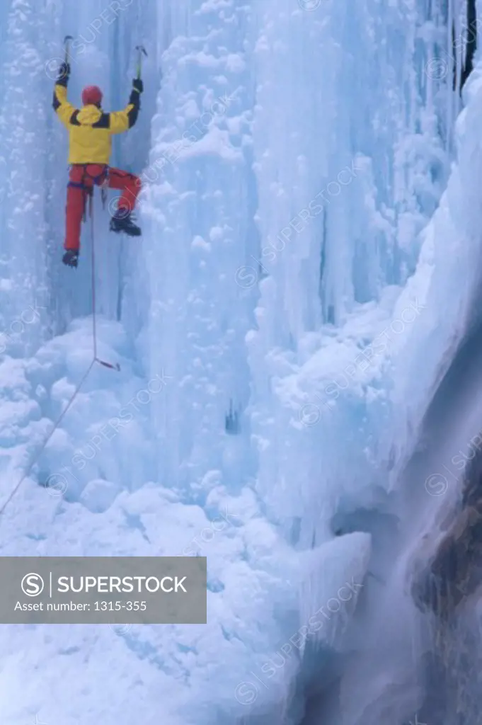 Rear view of a man climbing an ice covered cliff