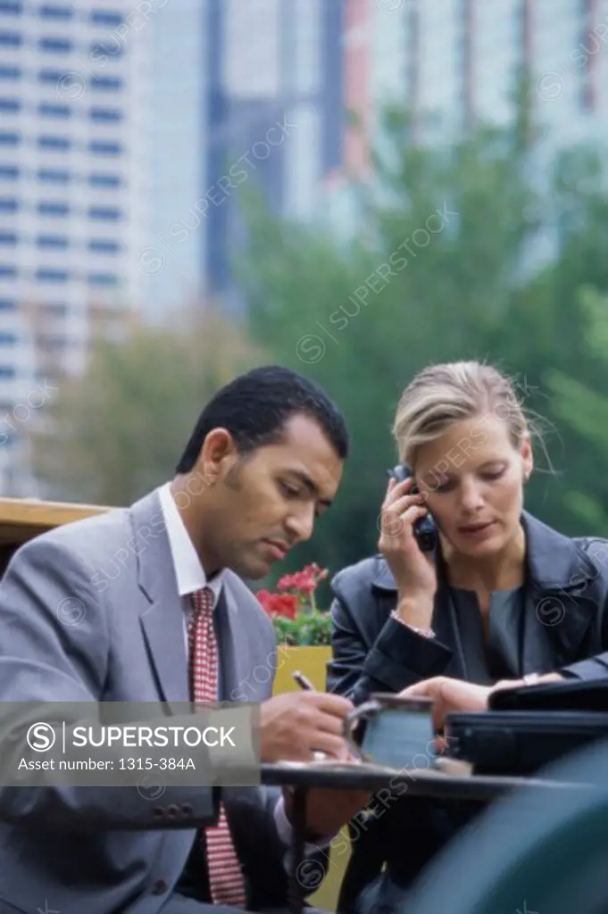 Businesswoman talking on a mobile phone with a businessman sitting beside her