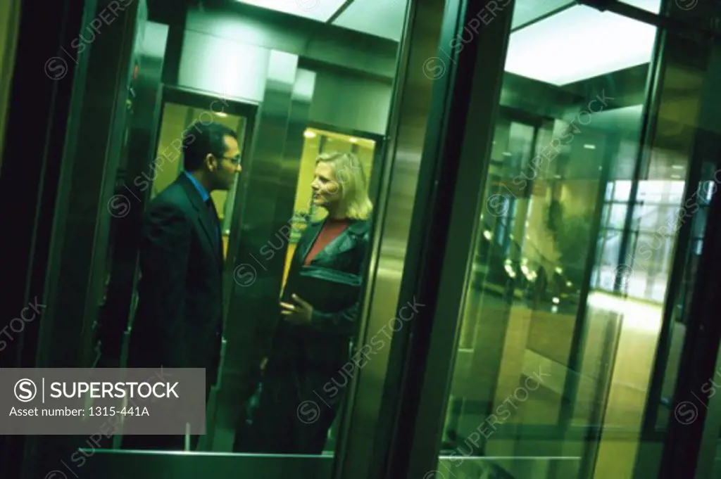 Side profile of a businessman and a businesswoman talking to each other in an elevator