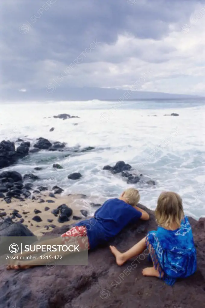High angle view of a brother and sister resting on a rock, Maui, Hawaii, USA