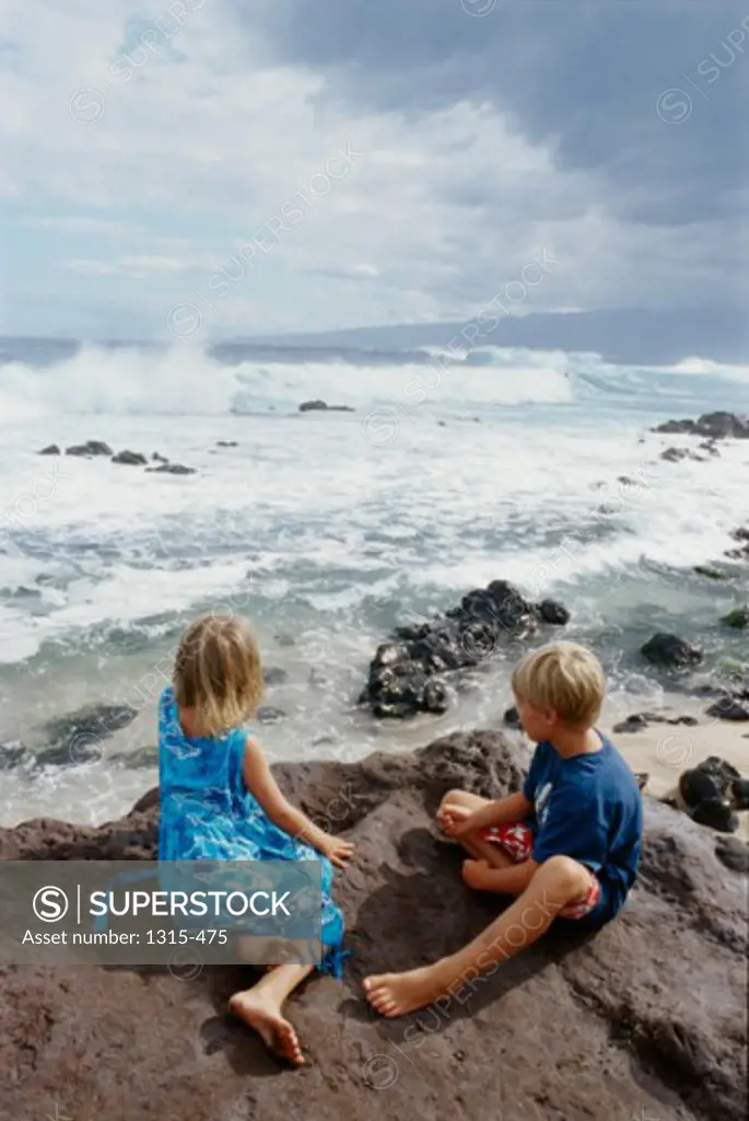 High angle view of a brother and sister sitting on a rock, Maui, Hawaii, USA