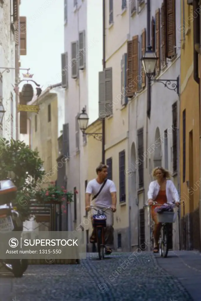 Young couple riding their bicycles on the road, Cremona, Italy