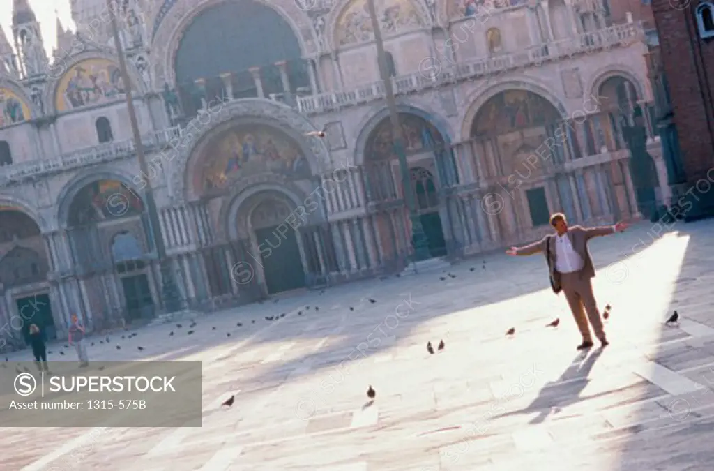 Mature man standing with his arms outstretched in front of a basilica, Basilica di San Marco, Venice, Italy