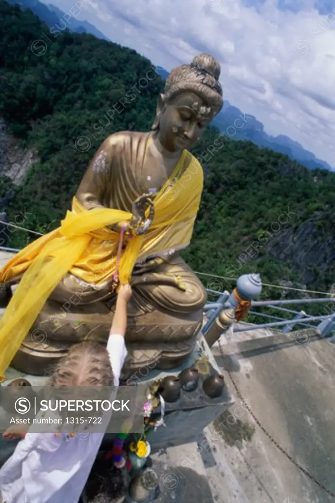 High angle view of a boy touching the statue of Buddha, Thailand