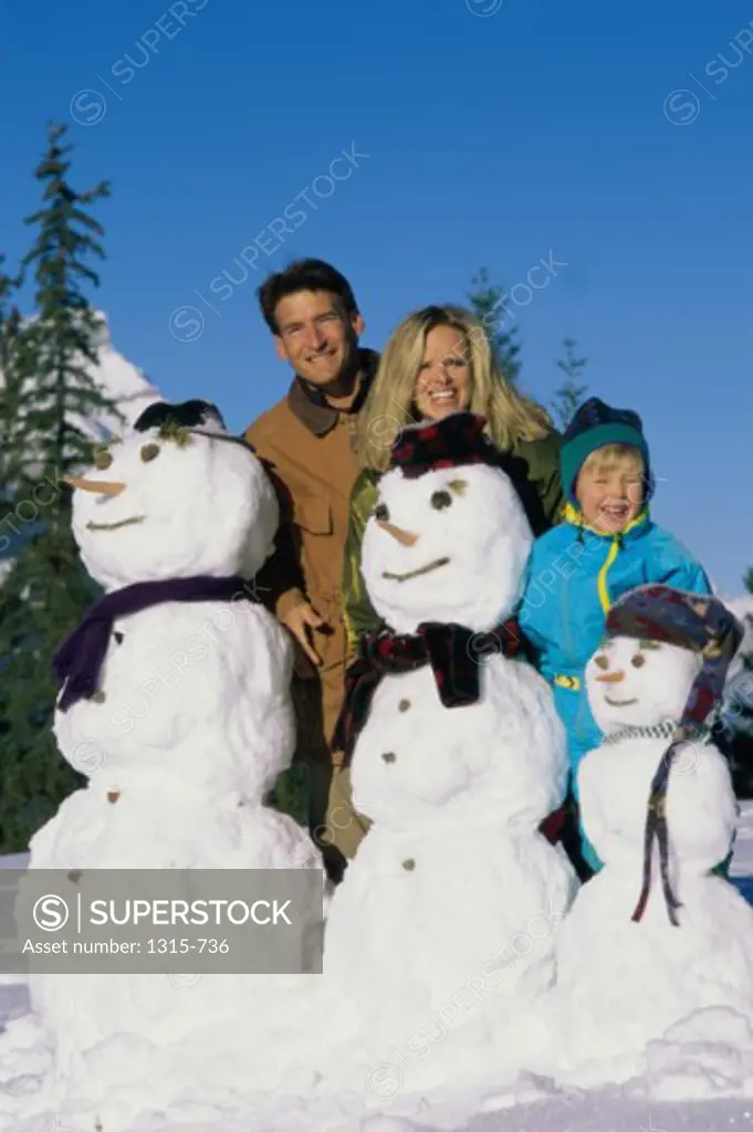 Portrait of parents with their son standing behind snowmen, Banff National Park, Alberta, Canada