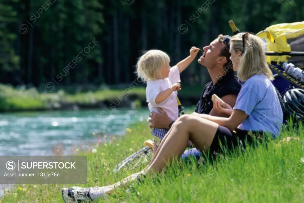 Side profile of parents with their daughter sitting at a riverbank