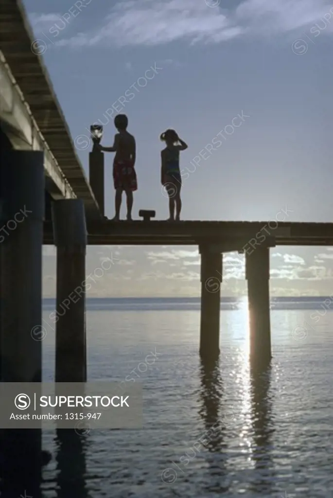 Silhouette of a brother and sister standing on a pier, Huahine, French Polynesia