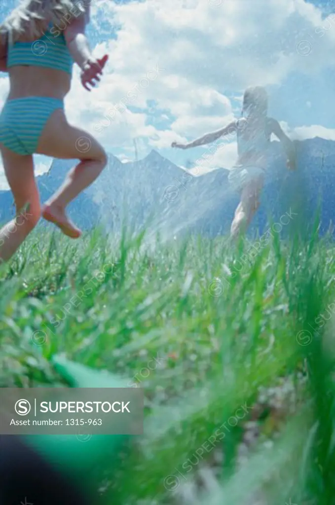 Two girls running in a sprinkler spray on a field, Banff National Park, Alberta, Canada