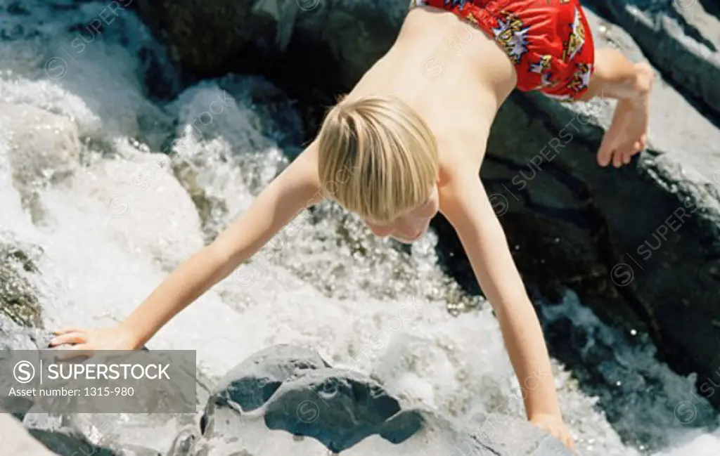 High angle view of a boy balancing on rocks across a stream
