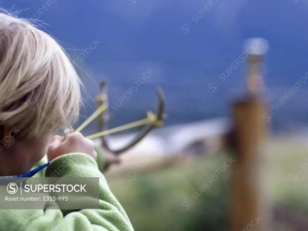 Rear view of a boy aiming with a slingshot
