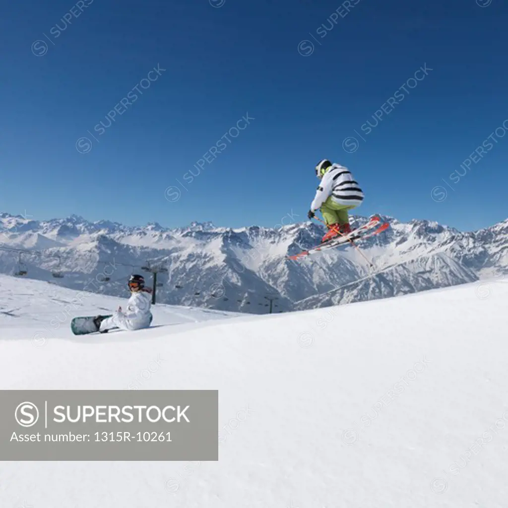 Italy, Piedmont, Jafferau, Teenage skier jumps over snowy ridgecrest, shows off in front of snowboarder
