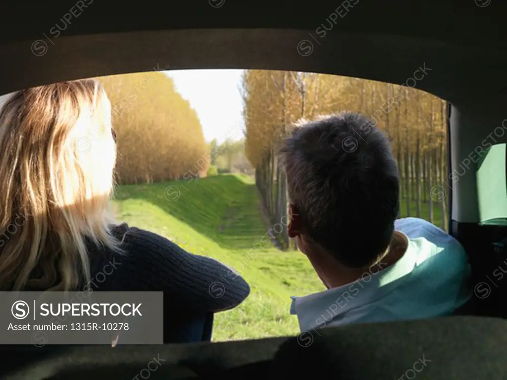 Italy, Piedmont, Couple look out from car interior to raised dike, planted forest