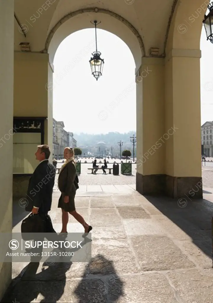 Italy, Turin, Business couple walk through porticos in front of piazza