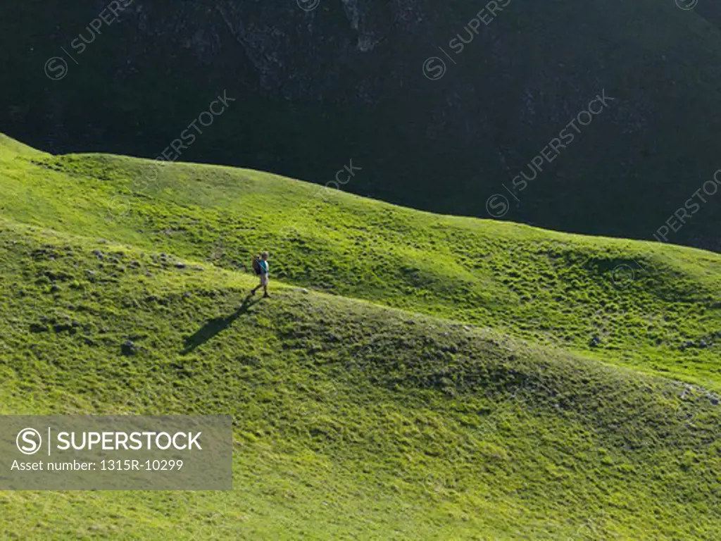 Italy, Piedmont, Hiker descends green mountain meadow