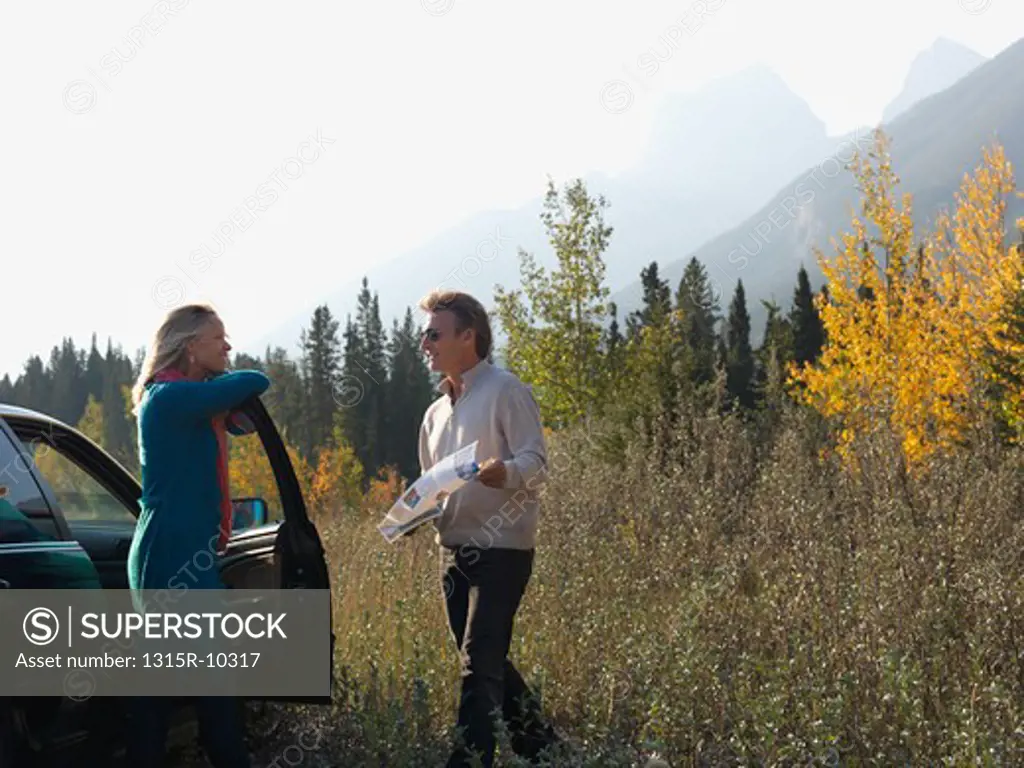 Canada, Alberta, Couple looking at map beside car in autumn meadow
