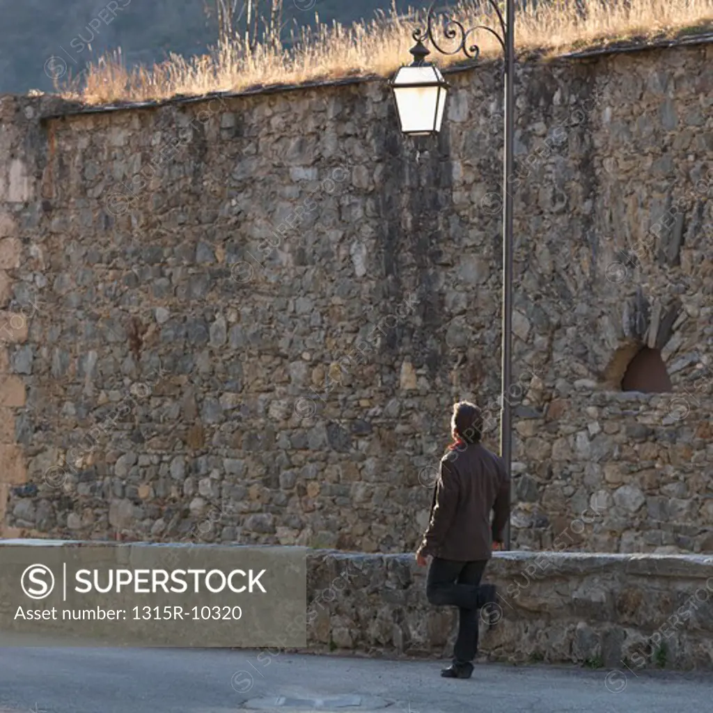 Italy, Piedmont, Cuneo, Man walking beside medieval wall